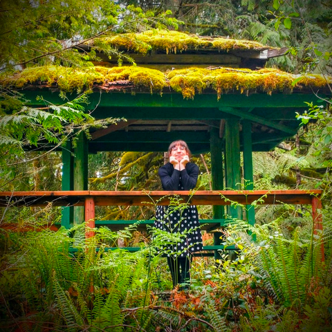 A luscious green photo with me in the middle of it. I'm in a black and white polka dot dress with a sweater top, leaning on a mossy railing with both elbows and my chin resting in my hands. My eyes are closed, and I'm smiling enormously. To every side of me is greenery, ferns, trees, and a gazebo behind me with it's roof covered in layers of moss