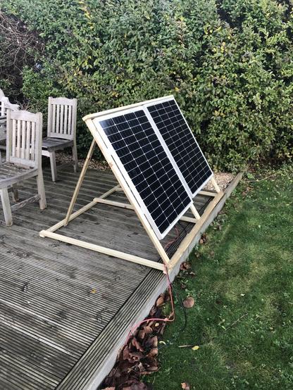 Two 120W solar panels in a wooden frame set at winter angles. They sit on a wooden deck with a little bit of lawn visible (grass and clover)