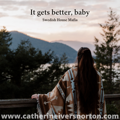 Woman wrapped in native blanket looks out over a railing to the view across a body of water to the lush pine tree covered hillside on the other side. Caption reads "It gets better, baby" (Swedish House Mafia)