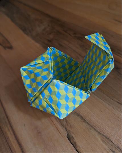 An open origami paper box cube where each side has a squat pyramid atop, in a blue/yellow cube-patterned paper.