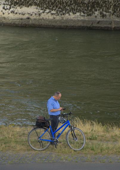 man looking at his phone, next to his bike, right by the water