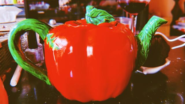 Une théière tomate de profil : la Hanse, capuchon et le bec sont des feuilles vertes et le corps une tomate très charnue rouge. En céramique. Autour c'est cradeau désolé
