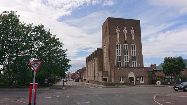 A brick church with cream stone detailing.  It's very blocky in design, looking almost Minefraftian.

It has a tower and the front has three vertical windows, each topped with a statue relief set into the brickwork.