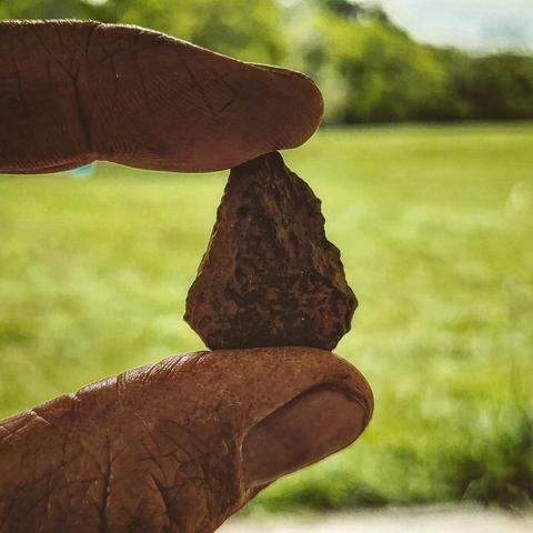 A projectile point is held in between a thumb and forefinger.