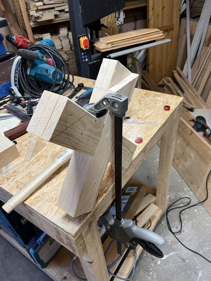A wooden X is clamped to a workbench. There are markings on the ends of the X designating where it has to be cut.