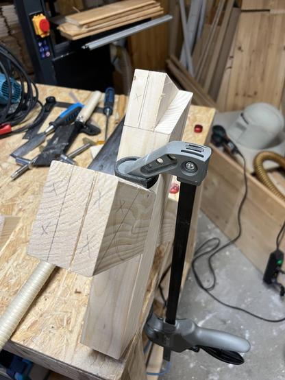 A wooden X is clamped to a workbench. There are markings on the endgrain of the X dividing it in three equal parts, designating where it has to be cut.