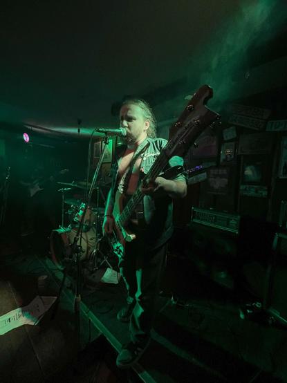 Picture of me on the stage, with a greenish light. I am holding a Rickenbacker bass and singing into the microphone.