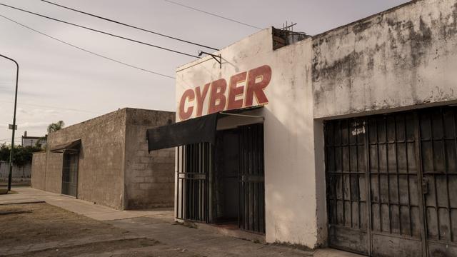 Empty street lined with buildings. The building in the middle of the photo has a dark awning and is painted white with the word CYBER painted in red.
