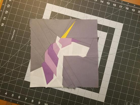 Foundation Paper Pieced Block of a white Unicorn on a grey background. Horn is yellowish-goldish; mane is alternating lilac and purple. Unfinished measurement is a very rough 10 inches.