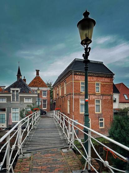A pedestrian bridge with a street lamp leads towards several typical Dutch houses in the background. Taken in Appingedam, the Netherlands.