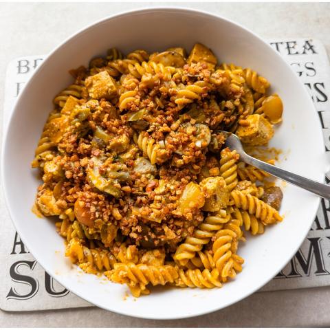 A white bowl of pasta with veggies in a red sauce