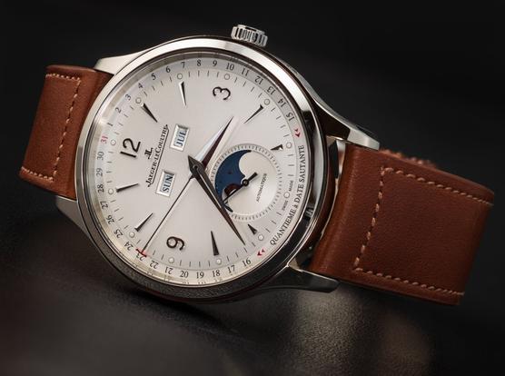 A Jaeger-Lecoultre Master Control Calendar watch (with an off-white dial, full calendar, and a moonphase display within the small-seconds dial at six o'clock) is lying on its 9:00 side.  The watch has a medium-brown leather band.