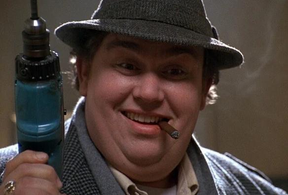 A close-up shot of Uncle Buck holding a drill in his right hand as he looks at Bug (who is off-camera in front of him).  Buck has a psychotic look on his face while he smokes a custom-made cigarette.