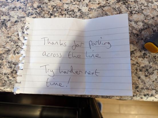 Hand written note saying: 
“Thanks for parking across the line Try harder next time!”