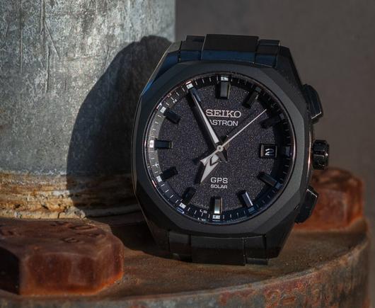 A tighter crop from the other photo in this post: a black wristwatch atop a rusted metal surface next to a rising silver metal pipe