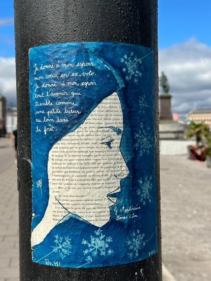 A piece of street art consisting of a woman’s face painted in blue over what appears to be a page from a book in French. In the upper left, a poem is handwritten in white; text in the bottom right attributes it to G. Appolinaire.