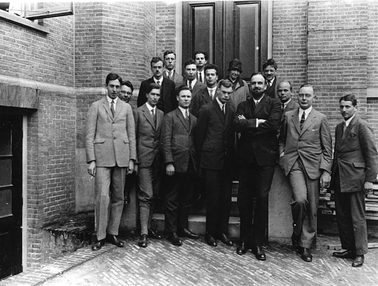 Public domain photograph from 1926 with a group portrait of a bunch of famous physicists on the entrance stairs to Kamerlingh Onnes's laboratory in Leiden. There are sixteen people in three rows, fifteen men and one woman, Tatyana Afanasyeva. Among the men we find Fokker, Dirac, Ehrenfest, Oppenheimer and Uhlenbeck.