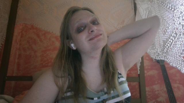 Adrienne with her hair down. She has her elbow up with her hand pressed to the back of her head. She's wearing black eyeshadow caked around her eyes. Photo taken August 15th, 2023.