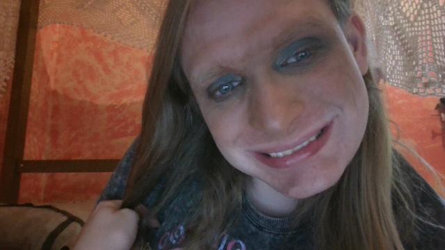 Adrienne grinning at the camera. She's wearing jade-toned eyeshadow and contour across the nose, cheekbones, and underneath the eyes to blend out the excess eyeshadow. Photo taken August 17th, 2023.