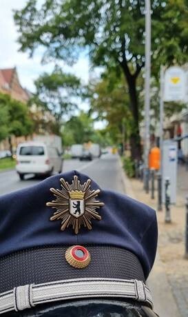 Im Vordergrund eine Mütze der Polizei Berlin. Unscharf im Hintergrund eine Straße.