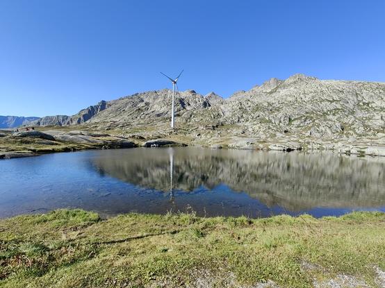 Pequeño lago de montaña alpino con un aerogenerador de fondo en el paso de St. Gotthard