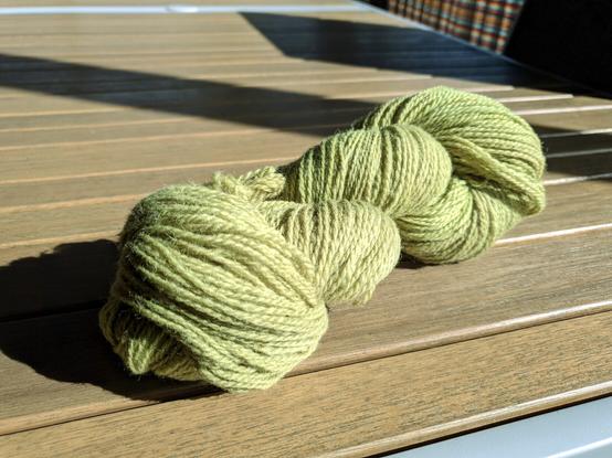 Green/yellow skein of yarn on a wooden table.