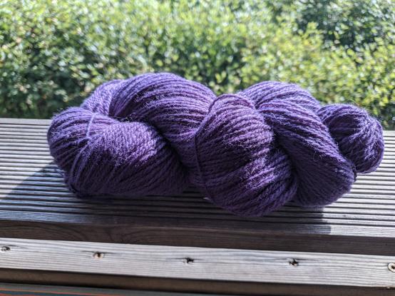 Purple yarn skein on wood, green background.
