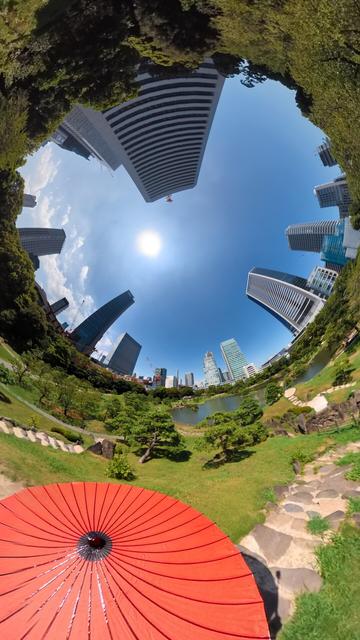 An inverted fisheye image of the Kyū Shiba Rikyū Gardens in Tokyo, with blue sky in the middle and gardens all around the perimeter, and the top of a large red paper umbrella in the lower foreground.