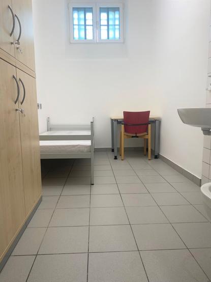 Blick in ein Zimmer im sogenannten Maßregelvollzug. Mit Schrank, Bett, Tisch, Stuhl und Waschbecken ist es einfach aber funktional eingerichtet.