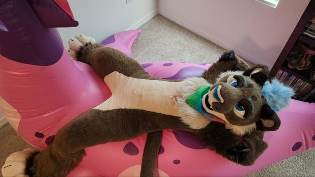 Lioness fursuiter laying on back of giant pink sea dragon inflatable