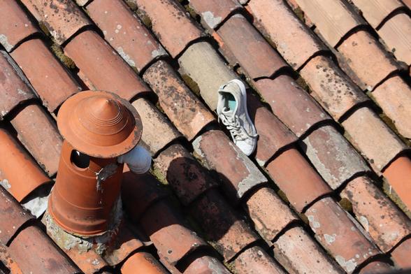 Una scarpa da ginnastica su un tetto di tegole accanto a un camino.