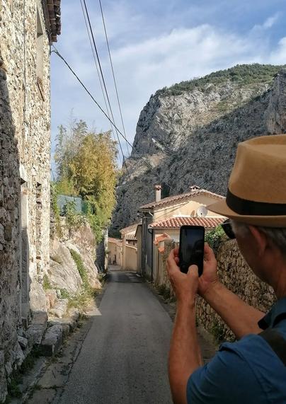 Der Mann mit Hut knipst Häuser vor Felsen.