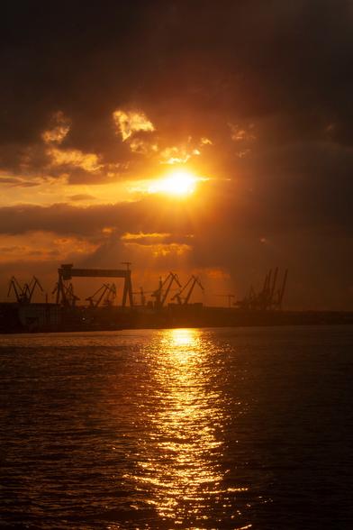 Sunset over shipyard with a lot of godrays piercing the clouds.