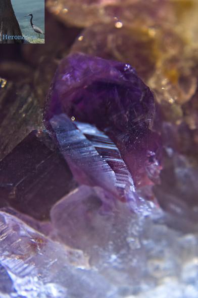 A macro, close-in photograph of the termination point of a purple amethyst crystal, rising out of the jumbled crystal “floor.” Directly beneath the peak, the crystal beings to turn white.