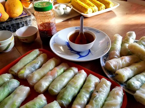 A tray & plate, filled with Vietnamese prawn & pork salad rolls. A bowl of nuoc cham sauce is on a plate, with Chinese soup spoon in it. Chili paste sauce is behind the nuoc cham.