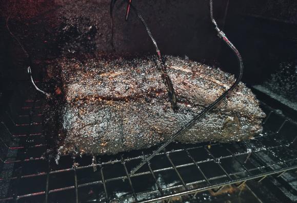 A large hunk of dark crusted meat on a mesh rack in a crusty smoker with several thermometer probes stuck into it and around it.