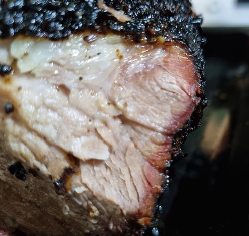 A cross section of cooked pork with a dark crusted exterior and a red "smoke ring" visible under the crust.