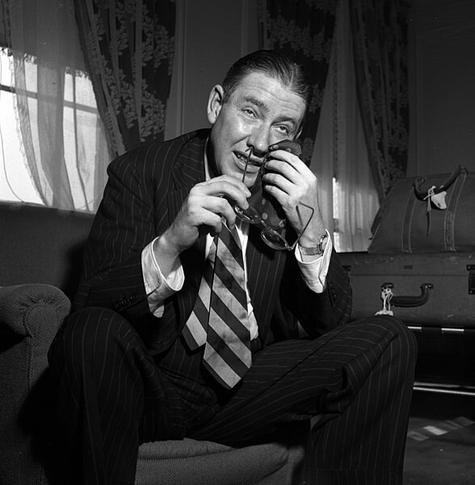 Foto pri Nash je 1949. Li sidas en fotelo, klinas antaŭen, tenas okulvitron per la dekstra mano, uzas maldekstran por viŝi sian vizaĝon per malgranda tuko. Li estas vestita en pingle striata kompleto kaj larĝe striata kravato.