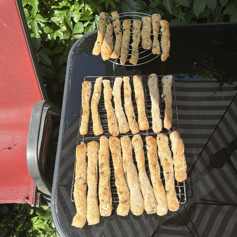 Closeup from above of 26 cheese sticks, resting on two cooling racks. They have a perfect golden colour and I tested one before I put the rest in the freezer. So I know they'll taste fine too.