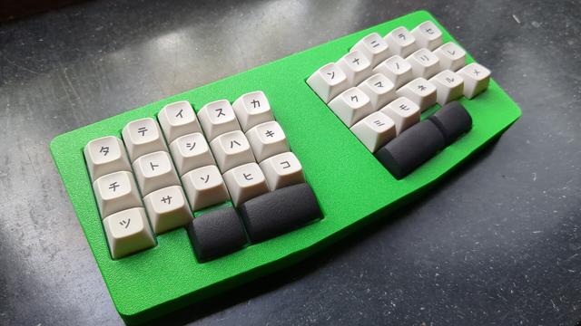 le chiffre mechanical keyboard with a very green case, white mt3 katakana keycaps for the alphas and black convex DES caps for the thumbs