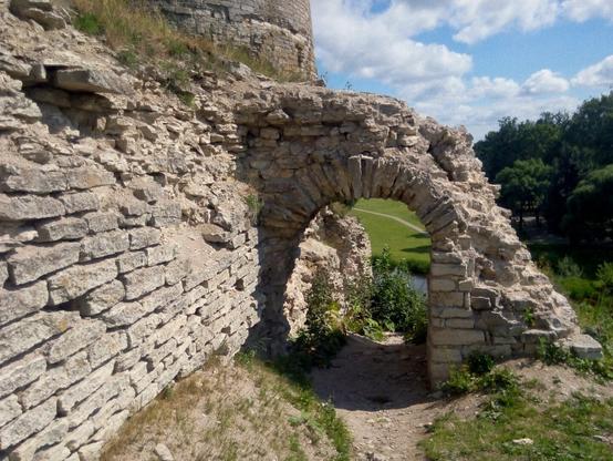 Path goes through a stone arch, part of the ancient stone wall is visible on the left, gray stones, far away trees is visible