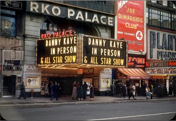 color photo of New York's RKO Palace Theater. circa 1950s. Marquee lit with gold bulbs. RKO PALACE lit in red above marquee. Marquee states "DANNY KAYE IN PERSON & ALL STAR SHOW." Next door, right, is large red,white &yellow sign for "Joe DiMaggio's Club WNBT Channel 4"