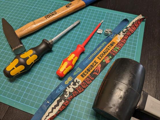 Opened wristbands of CCCamp2019, 36c3 and CCCamp23 next to each other. Next to them two screw drivers, a metal and a rubber hammer.
