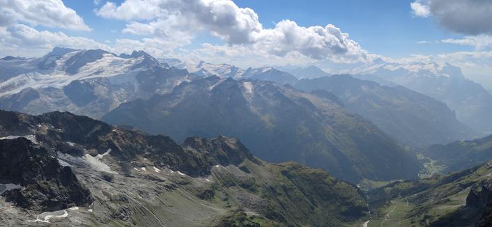 Looking down at the valley at the bottom of the glacier. In the background, high mountains, other glaciers, blue sky, white clouds... A classic Swiss mountains landscape.