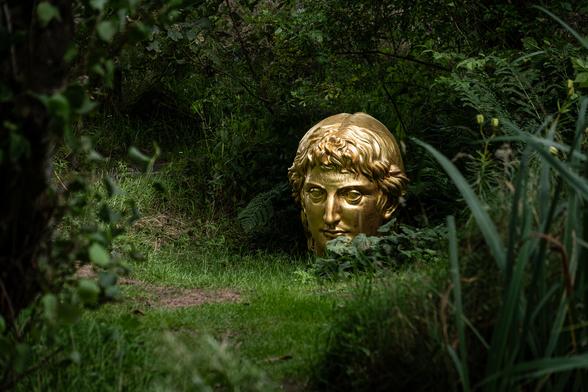 Artwork of golden Apollo's head amongst vegetation