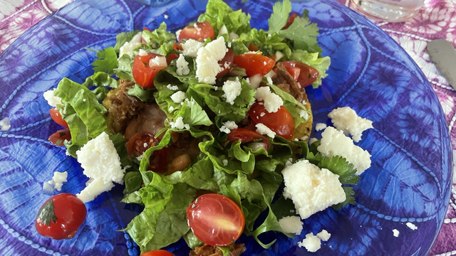 Tostada with beans, barbecue Mexican pork, bright green lettuce, bright red grape tomatoes and bright white  Mexican cheese