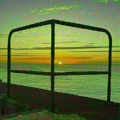 Au premier rang une rembarre qui forme 4 quartiers. 
Derrière la mer. Au loin le soleil couchant et un ferry sur l’horizon