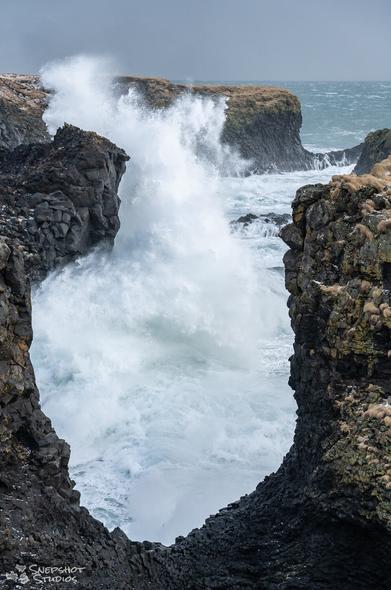 Look through a gap in cliffs at the seaside with a huge wave crashing with white spray