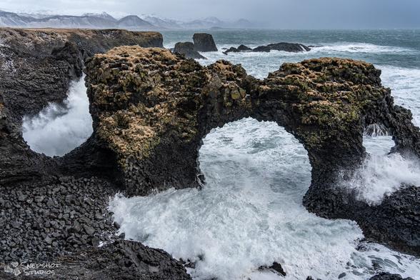 Look at and through an arch shaped seastack with waves coming through the openings