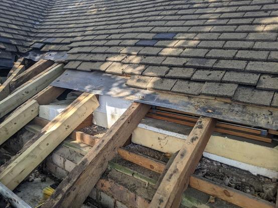 A picture of the roof with the tiles, battens, that hold the tiles in place and the felt removed to reveal the insulation above the ceiling inside the roof. New timber has been fixed to the side of the damaged timbers of the rafters to bring the roof back up to the correct level. Many of the battens had completely rotted out leaving  the tiles to slump.